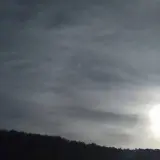 Słońce przebija się przez cienką, włóknistą warstwę cirrostratus chmura, oświetlając sylwetkę lasu na wzgórzu.