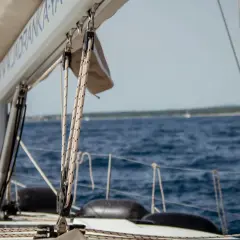 Żagle i liny na jachcie, w tle błękitne chorwackie morze i linia brzegowa.