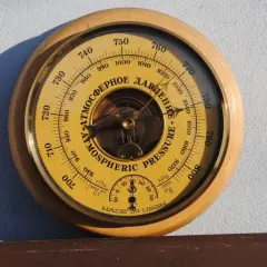 Barometr z tarczą w kolorze żółtym, wskazujący ciśnienie atmosferyczne w hektopaskalach. Wskazówka pokazuje wartość około 1010 hPa.