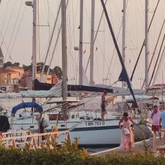 Ludzie na pomoście w marinie, wśród żaglówek. W tle miasteczko z wieżą kościelną, idealne do nawigacji terestrycznej.