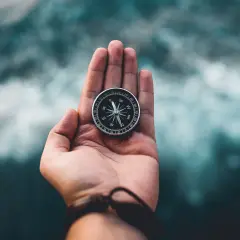 Dłoń trzyma kompas na statku, wskazując kierunek wśród wzburzonych fal.