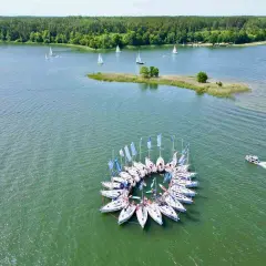 Wycieczka na Mazury 3 dni: żaglówki tworzą okrąg na jeziorze, w tle las i mała wyspa.