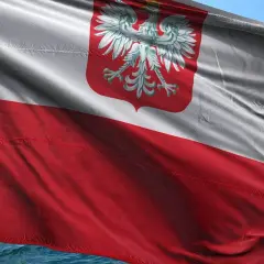 Flaga bandery w Polsce, biało-czerwona z orłem, powiewa na wietrze nad wodą.