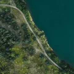Piękny brzeg Mazury z lotu ptaka. Droga wijąca się wśród zieleni nad turkusową wodą.