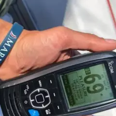 Dłoń z opaską "MARISTO" trzyma radio UKF ICOM IC-M930, wyświetlające nazwę "PLEASURE" i współrzędne.