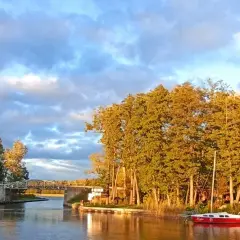 Złociste **Mazury jesienią**. Kanał, most, żaglówki i łodzie przy brzegu, wśród drzew w jesiennych barwach.