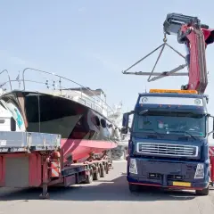 Ciężarówka z dźwigiem przygotowuje transport jachtu z przyczepy.