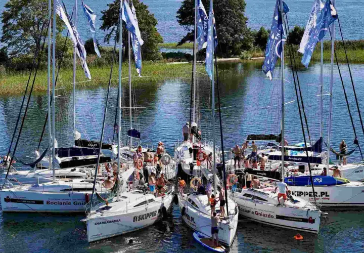 Grupa żaglówek na Mazurach, ludzie na pokładach, flagi z napisem "Na Mazury".