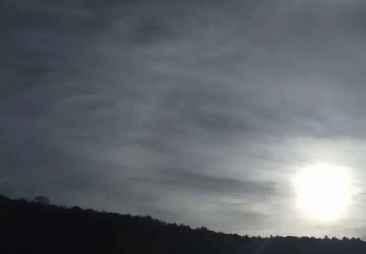 Słońce przebija się przez cienką, włóknistą warstwę cirrostratus chmura, oświetlając sylwetkę lasu na wzgórzu.