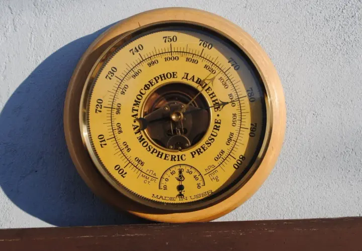 Barometr z tarczą w kolorze żółtym, wskazujący ciśnienie atmosferyczne w hektopaskalach. Wskazówka pokazuje wartość około 1010 hPa.