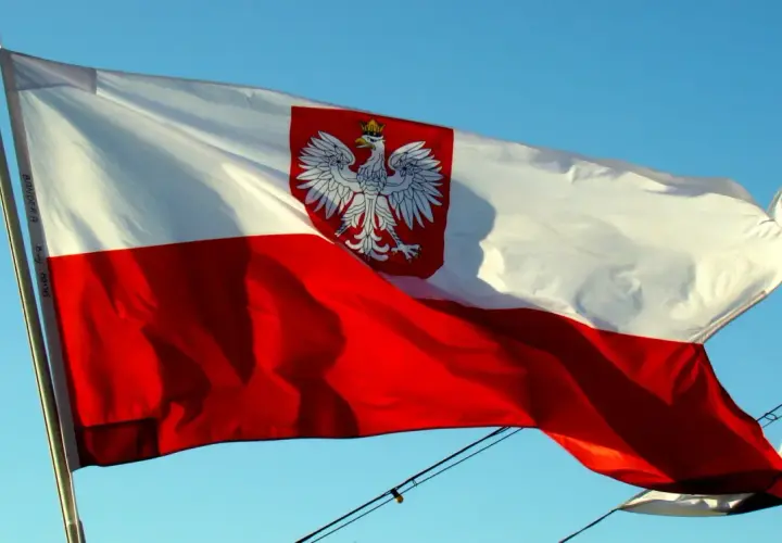 Flaga Polski z orłem w koronie powiewa na wietrze. Biało-czerwony znak bandery dumnie prezentuje się na tle błękitnego nieba.