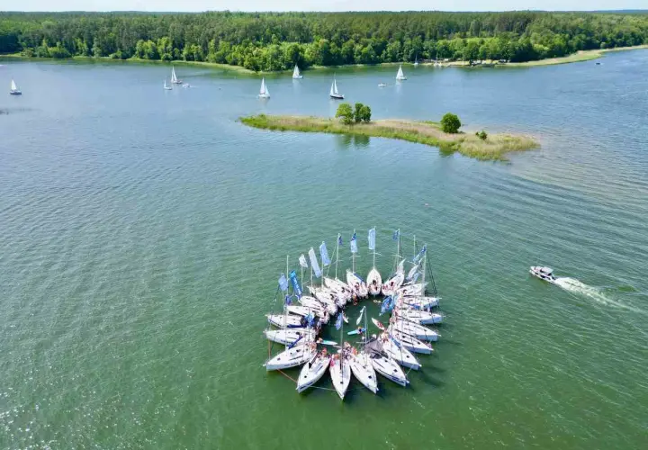 Wycieczka na Mazury 3 dni: żaglówki tworzą okrąg na jeziorze, w tle las i mała wyspa.