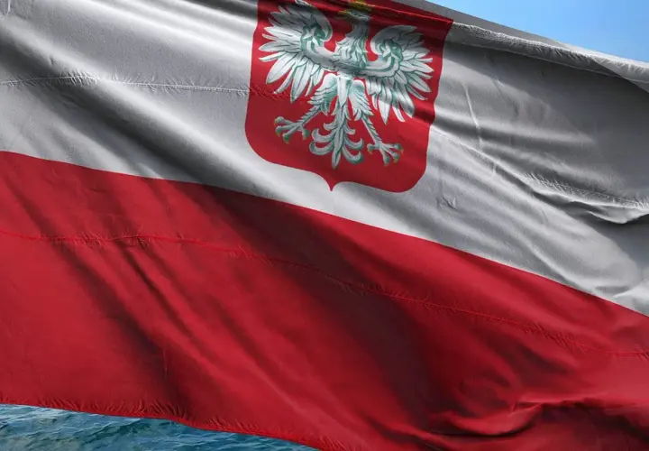 Flaga bandery w Polsce, biało-czerwona z orłem, powiewa na wietrze nad wodą.