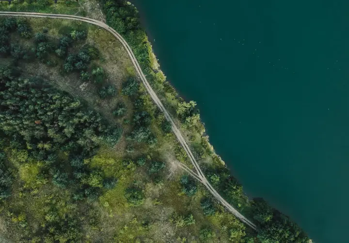 Piękny brzeg Mazury z lotu ptaka. Droga wijąca się wśród zieleni nad turkusową wodą.