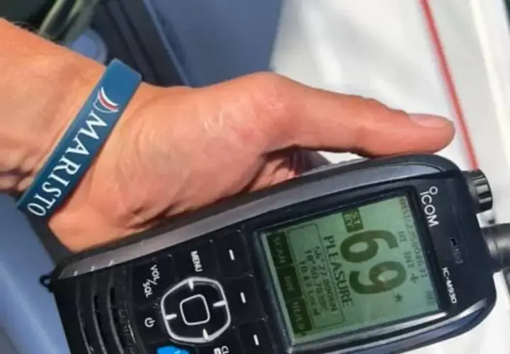 Dłoń z opaską "MARISTO" trzyma radio UKF ICOM IC-M930, wyświetlające nazwę "PLEASURE" i współrzędne.