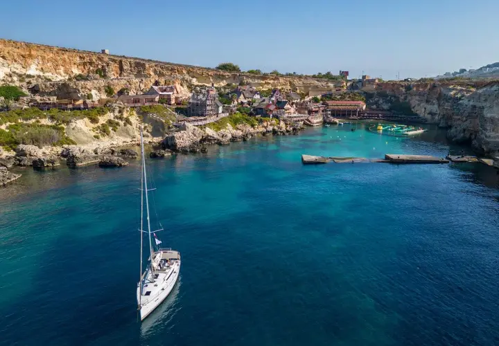 Malta: jakie morze! Biały żaglowiec kołysze się na turkusowych wodach zatoki, w tle kolorowe domki i klify.