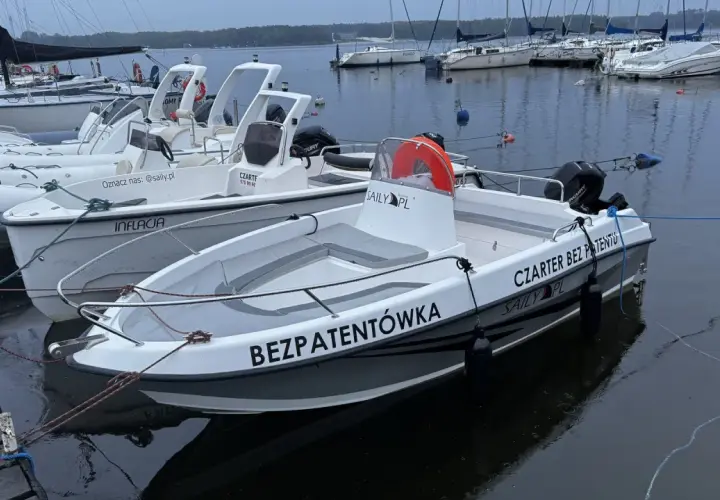 Łodzie motorowe cumujące przy pomoście, gotowe na czarter na Zalewie Sulejowskim. Jedna z nich ma napis "BEZPATENTÓWKA".