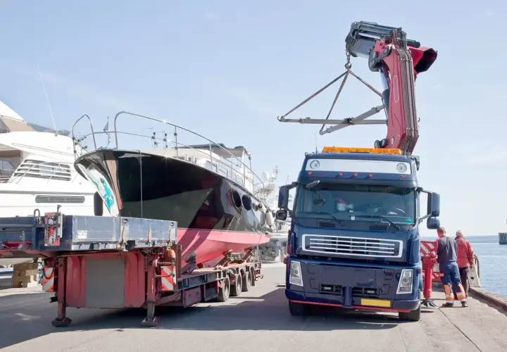 Ciężarówka z dźwigiem przygotowuje transport jachtu z przyczepy.