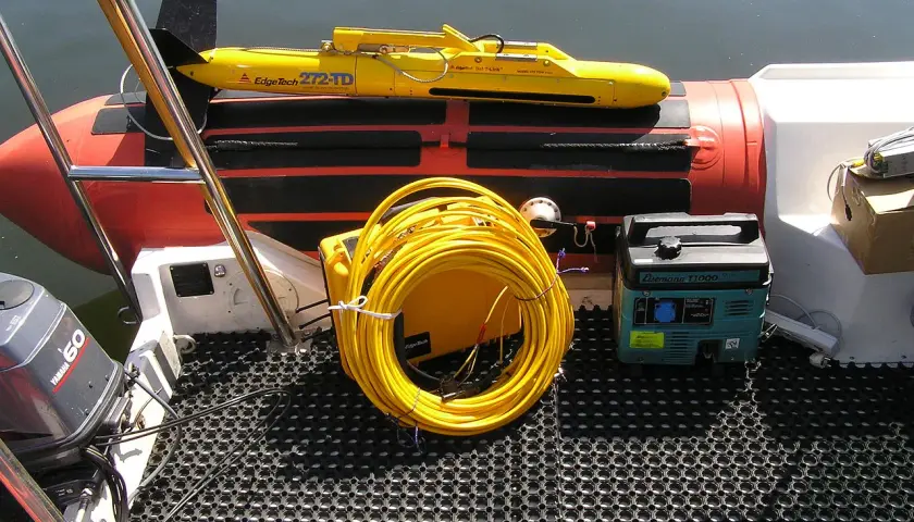 Żółty podwodny pojazd EdgeTech 272-TD, zwinięty kabel i agregat prądotwórczy na łodzi. To sprzęt do badań podwodnych, wykorzystujący technologię, która działa podobnie jak sonar.