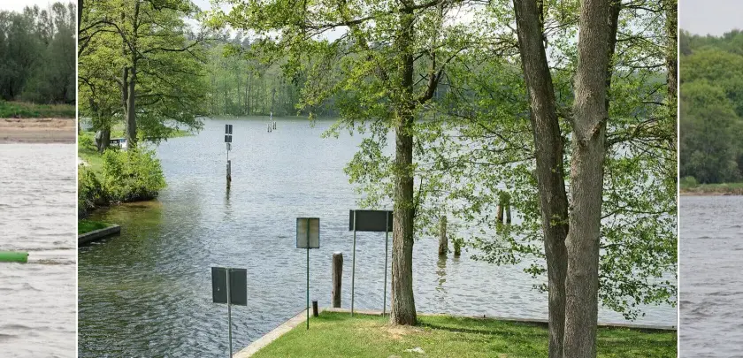 Zielona i czerwona boja, znaki dla żeglugi na spokojnej wodzie, otoczone zielenią drzew i brzegiem.