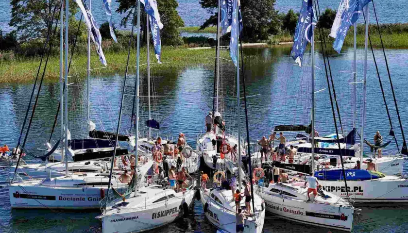Grupa żaglówek na Mazurach, ludzie na pokładach, flagi z napisem "Na Mazury".