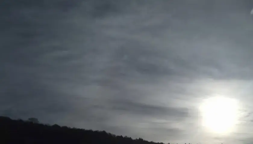 Słońce przebija się przez cienką, włóknistą warstwę cirrostratus chmura, oświetlając sylwetkę lasu na wzgórzu.