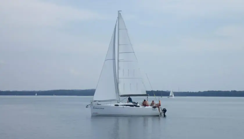 Biały jacht "Ramzesowa" płynie po spokojnym akwenie, przypominającym Marmara Morze. Na pokładzie widać kilka osób.