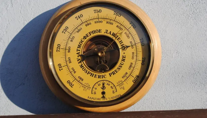 Barometr z tarczą w kolorze żółtym, wskazujący ciśnienie atmosferyczne w hektopaskalach. Wskazówka pokazuje wartość około 1010 hPa.