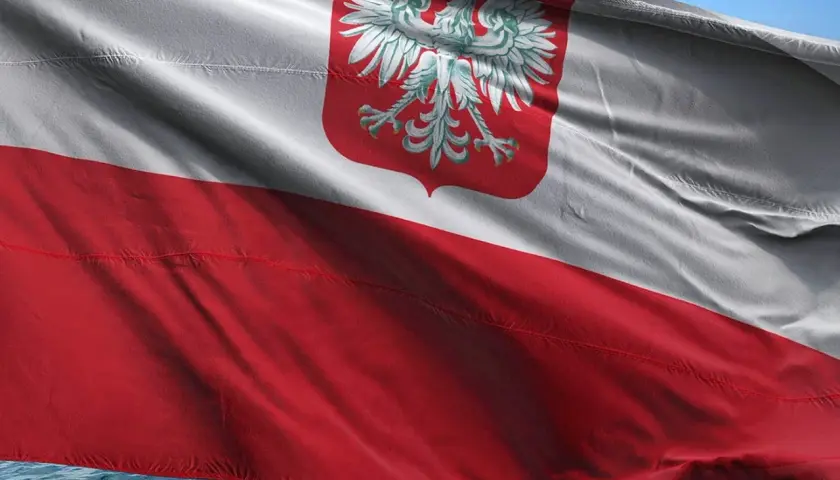 Flaga bandery w Polsce, biało-czerwona z orłem, powiewa na wietrze nad wodą.