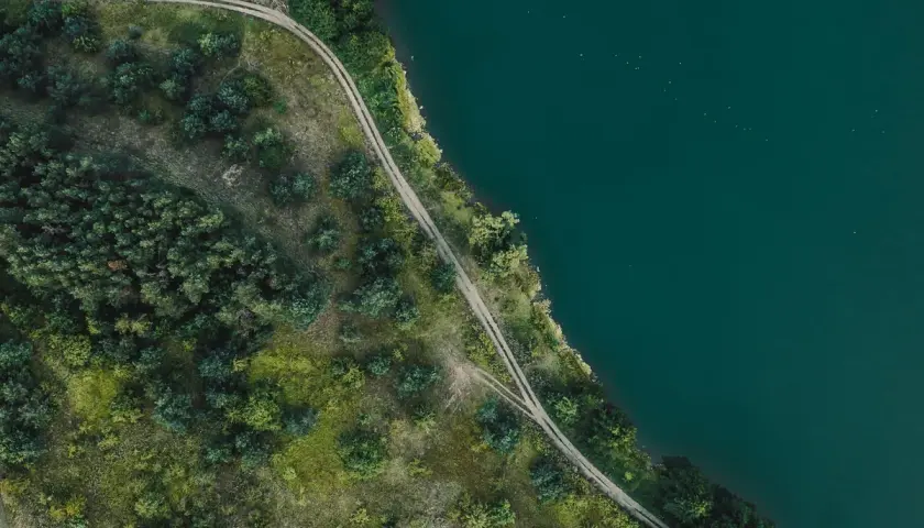 Piękny brzeg Mazury z lotu ptaka. Droga wijąca się wśród zieleni nad turkusową wodą.