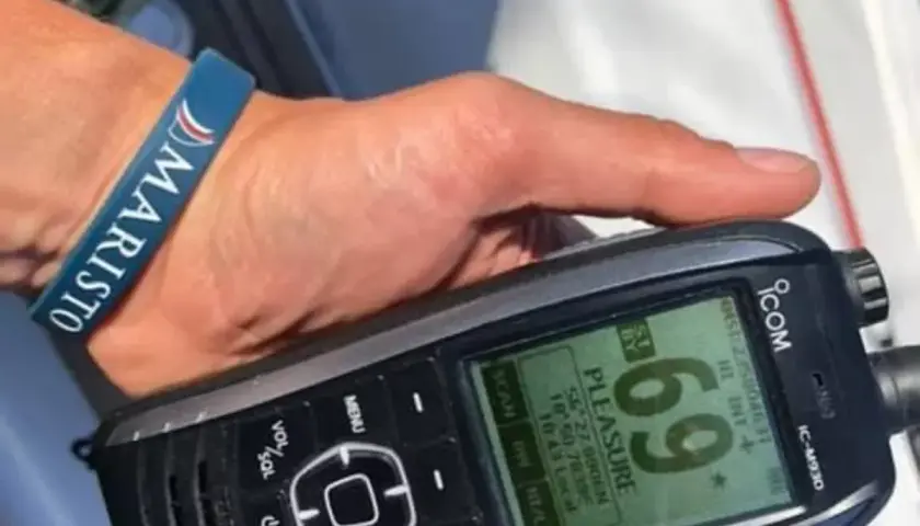 Dłoń z opaską "MARISTO" trzyma radio UKF ICOM IC-M930, wyświetlające nazwę "PLEASURE" i współrzędne.
