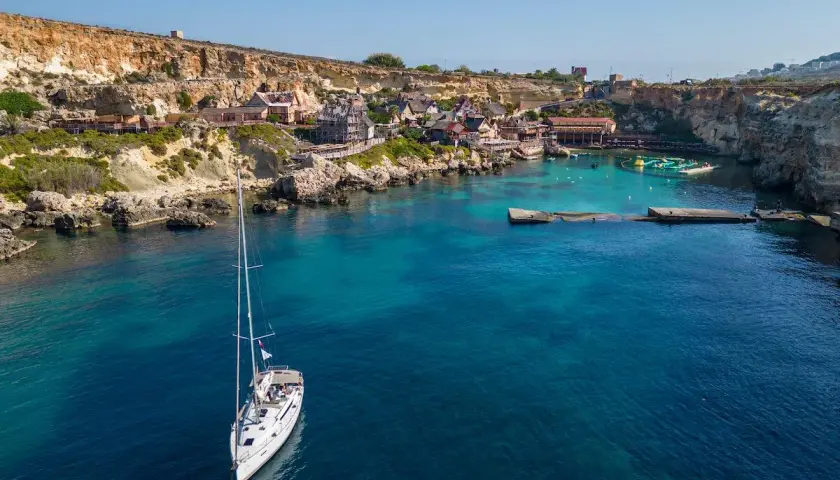 Malta: jakie morze! Biały żaglowiec kołysze się na turkusowych wodach zatoki, w tle kolorowe domki i klify.