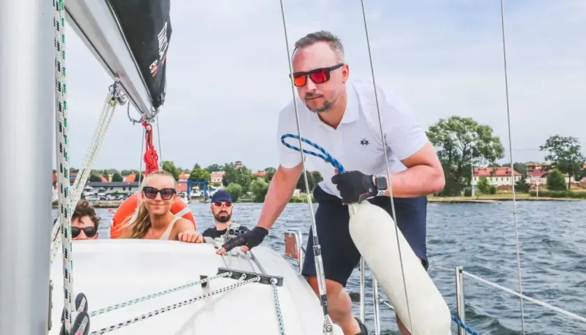 Ludzie na żaglówce cieszą się pięknymi **drogami wodnymi w Polsce**. Słońce, woda i przyjaciele to idealne połączenie.