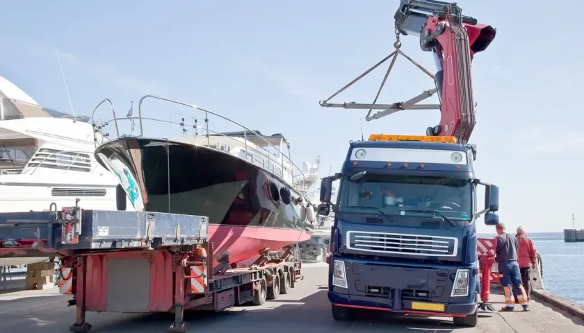 Ciężarówka z dźwigiem przygotowuje transport jachtu z przyczepy.