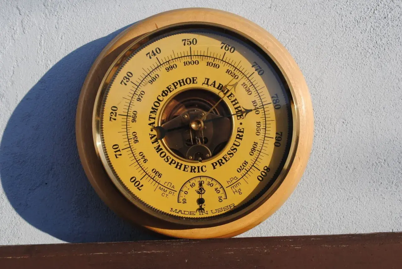 Barometr z tarczą w kolorze żółtym, wskazujący ciśnienie atmosferyczne w hektopaskalach. Wskazówka pokazuje wartość około 1010 hPa.