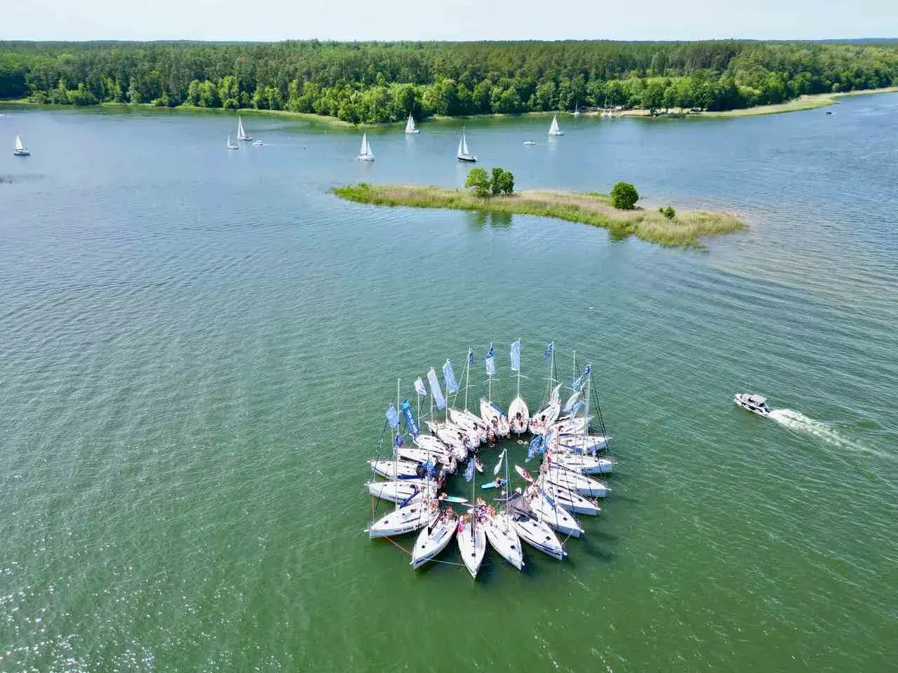 Wycieczka na Mazury 3 dni: żaglówki tworzą okrąg na jeziorze, w tle las i mała wyspa.