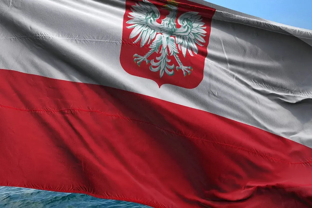 Flaga bandery w Polsce, biało-czerwona z orłem, powiewa na wietrze nad wodą.