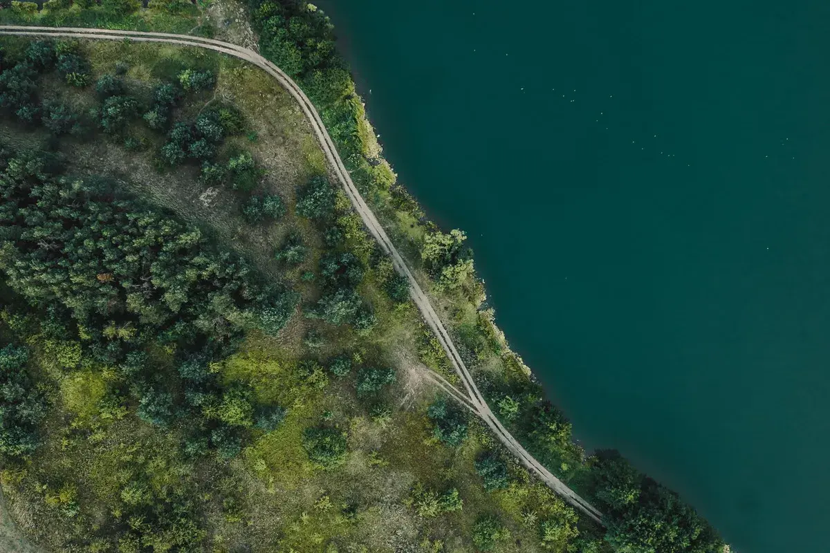 Piękny brzeg Mazury z lotu ptaka. Droga wijąca się wśród zieleni nad turkusową wodą.
