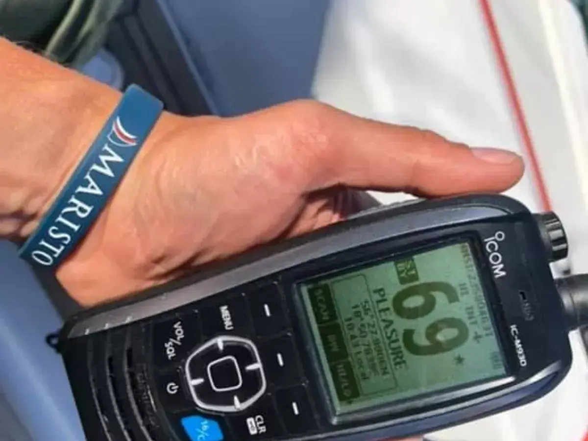 Dłoń z opaską "MARISTO" trzyma radio UKF ICOM IC-M930, wyświetlające nazwę "PLEASURE" i współrzędne.