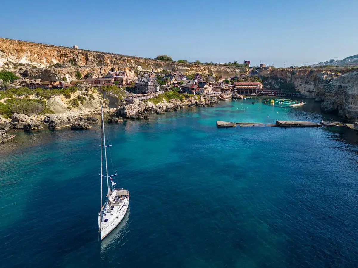 Malta: jakie morze! Biały żaglowiec kołysze się na turkusowych wodach zatoki, w tle kolorowe domki i klify.