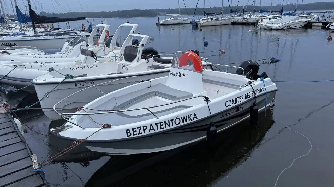 Łodzie motorowe cumujące przy pomoście, gotowe na czarter na Zalewie Sulejowskim. Jedna z nich ma napis "BEZPATENTÓWKA".