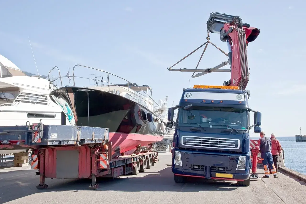 Ciężarówka z dźwigiem przygotowuje transport jachtu z przyczepy.