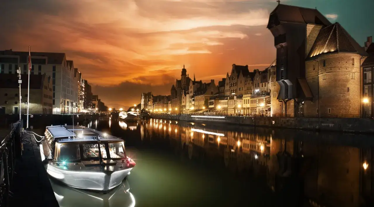 Wieczorna gdańsk wycieczka łodzią po Motławie. Widać zabytkowe kamienice, Żuraw i nowoczesną łódź.