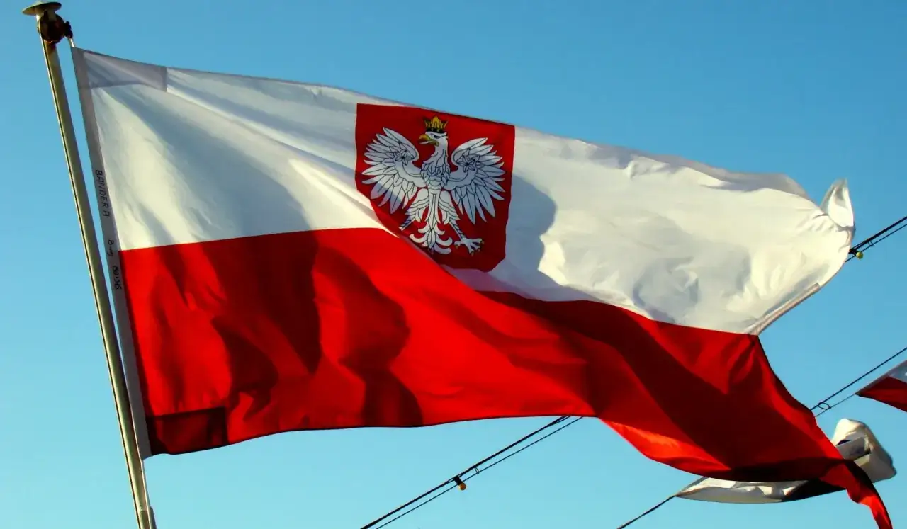 Flaga bandery w Polsce, biało-czerwona z orłem, dumnie powiewa na tle błękitnego nieba.