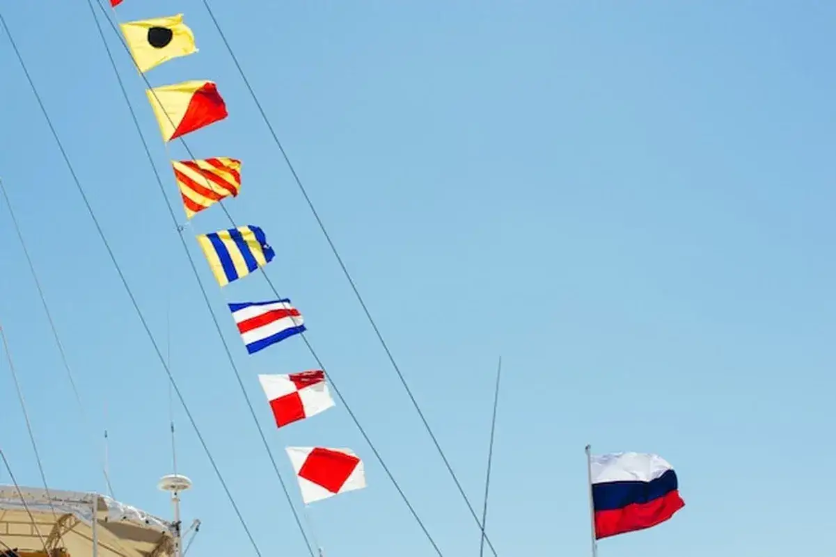 Sznur kolorowych flag sygnałowych wisi na statku na tle błękitnego nieba. Na pierwszym planie flaga Rosji.