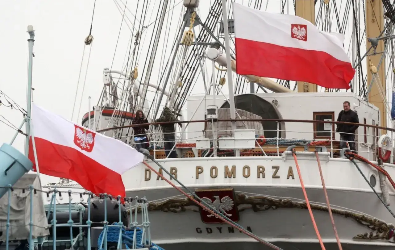 Dwa biało-czerwone flagi z orłem, czyli polski znak bandery, powiewają na tle żaglowca 
